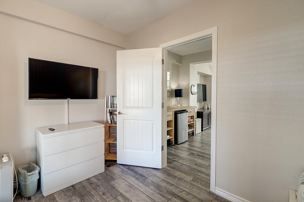 Your spacious bedroom flows seamlessly into the modern kitchen, featuring wall-mounted TV and thoughtful storage solutions for your comfort.