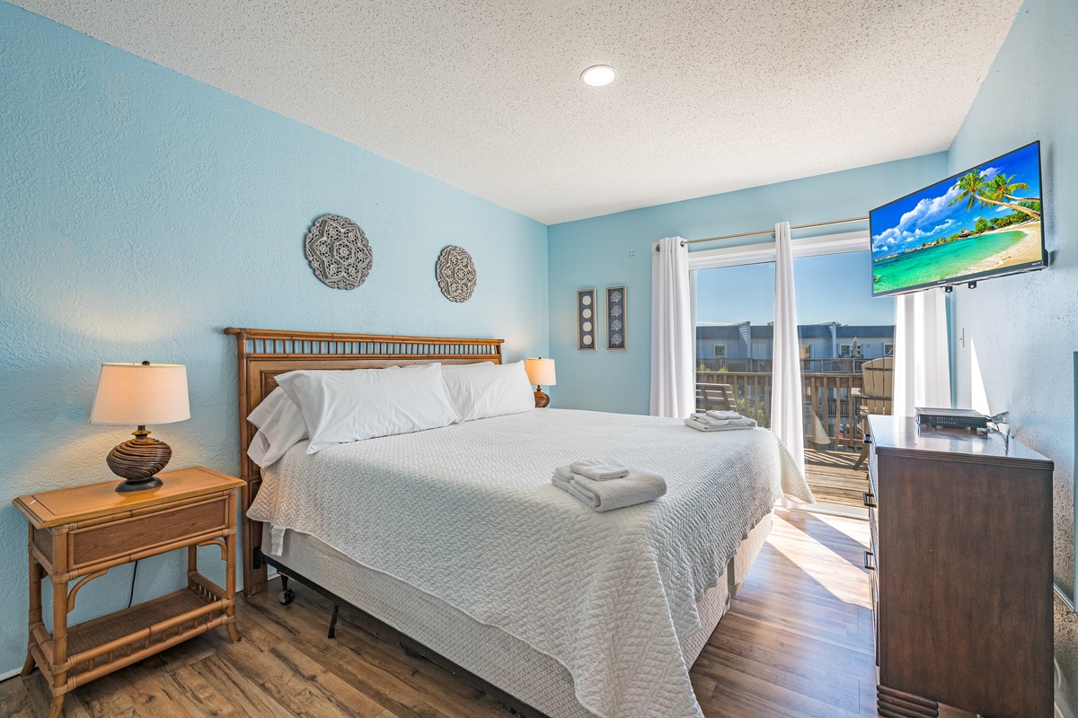 Wake up to serene coastal vibes in your bright bedroom, complete with a flat-screen TV and private balcony access for morning coffee.