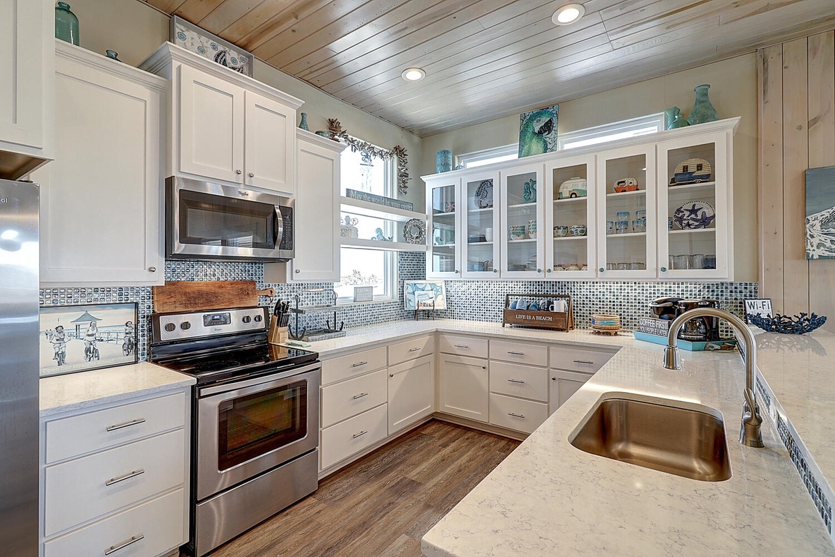 Your gourmet kitchen awaits with gleaming countertops, mosaic backsplash, and glass-front cabinets showcasing coastal treasures.