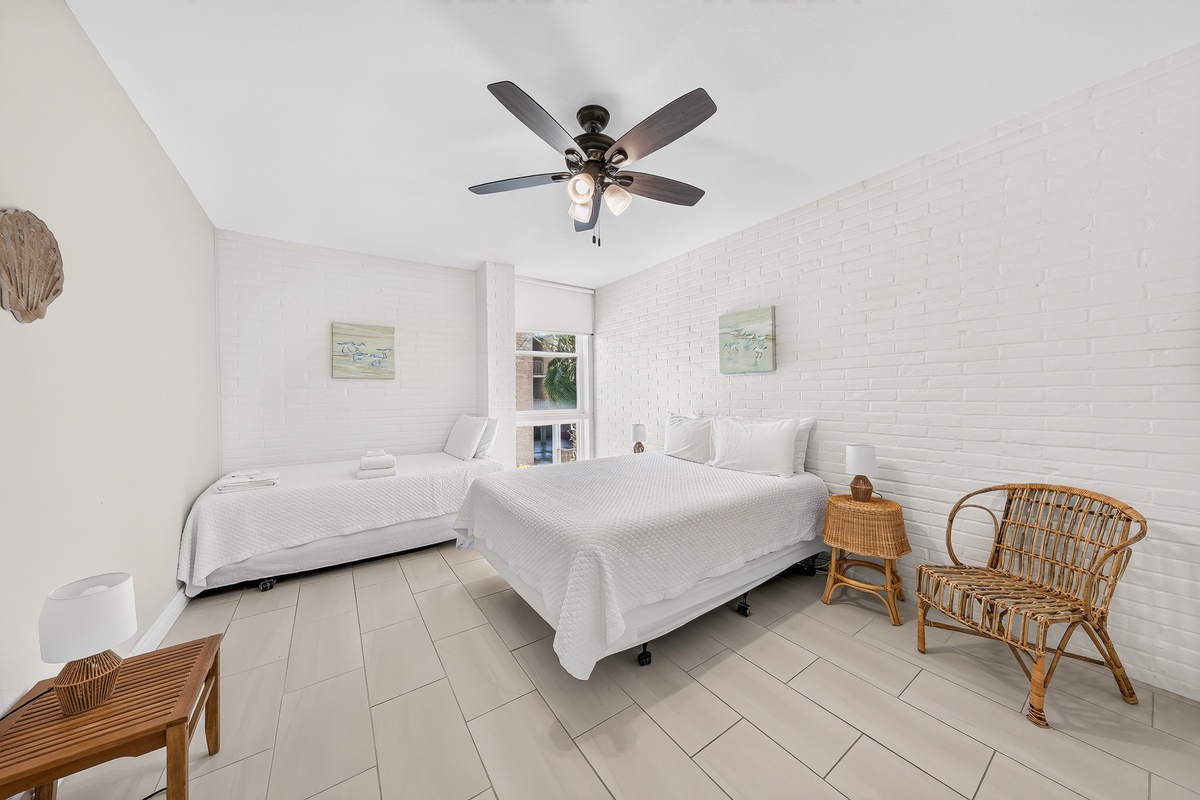 Drift off in this serene coastal-inspired bedroom with two plush beds, natural woven accents, and a gentle breeze from your ceiling fan overhead.