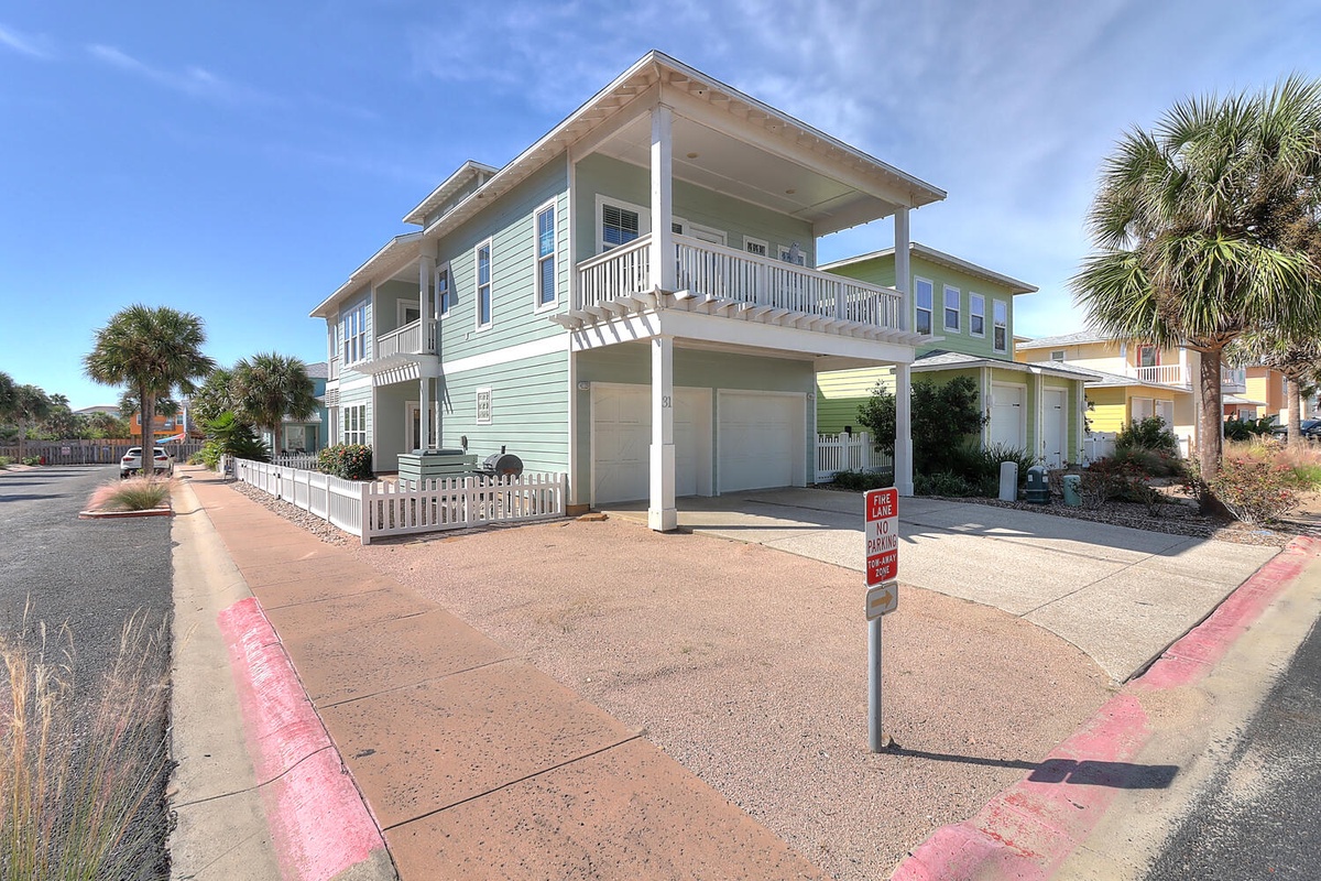 Charming two-story coastal home with covered balcony and palm trees in a beachside neighborhood.