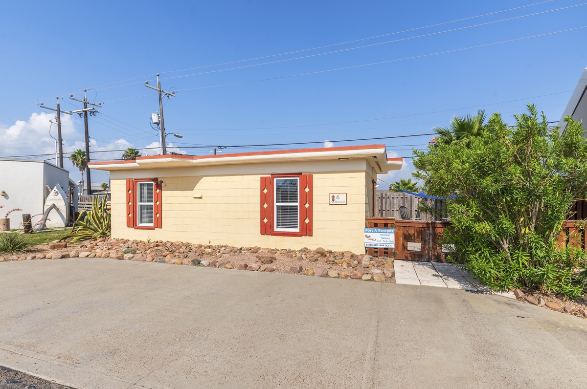 Charming coastal cottage with bright red shutters and tropical landscaping in a peaceful residential neighborhood.
