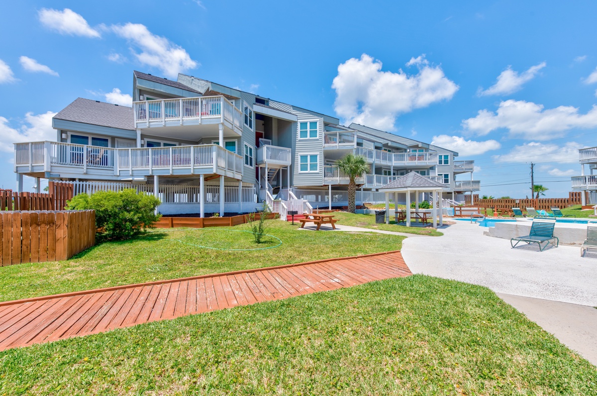 Modern coastal property featuring multiple balconies, landscaped grounds with wooden walkway, and poolside relaxation areas.