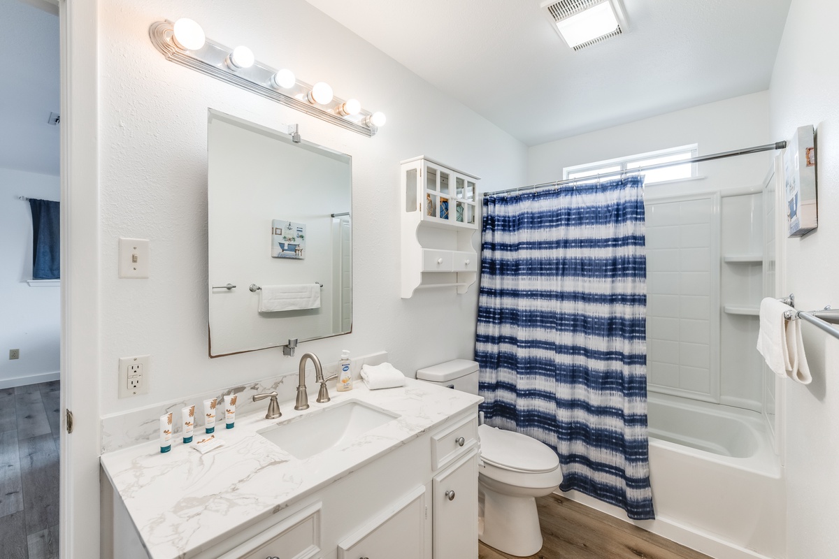 Your bright bathroom features marble counters, vanity lighting, and a relaxing tub-shower combo with coastal-inspired blue striped curtain.