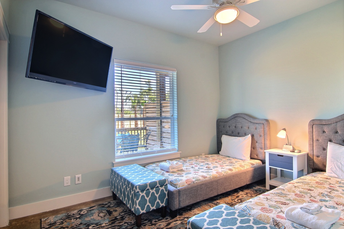 Your peaceful twin bedroom features plush beds, calming decor, and modern amenities like a wall-mounted TV and ceiling fan for ultimate comfort.