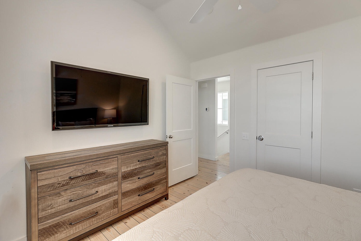 Relax in your bright, modern bedroom with wall-mounted TV and rustic dresser for convenient storage.