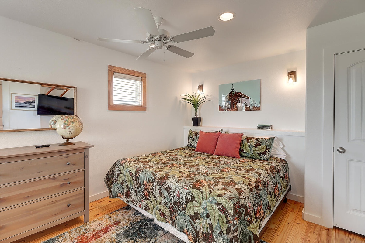 Rest in your cozy bedroom with tropical-themed bedding, warm wood floors, and thoughtful touches like the vintage globe and wall art.