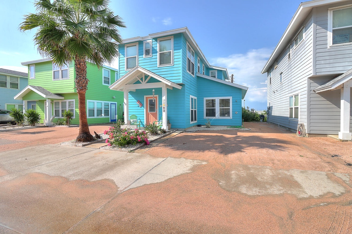 Bright coastal vacation homes with tropical palm landscaping and spacious paved parking areas in a charming beach community setting.