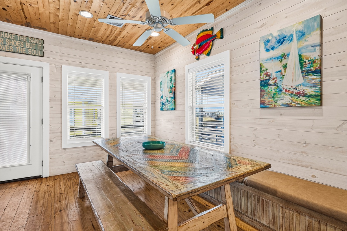 Gather around the rustic wooden table in this bright coastal-inspired dining space, where natural light streams through three windows and beach-themed art welcomes you to every meal.