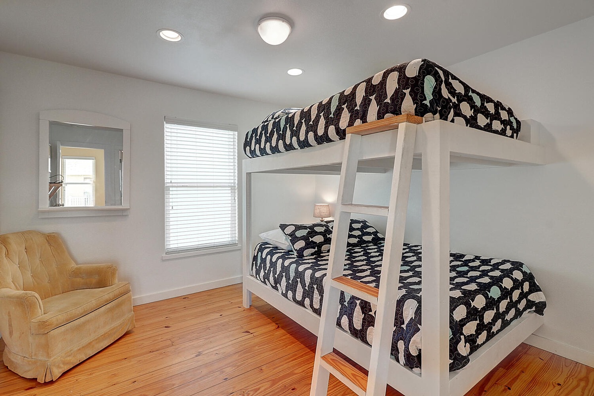 Rest easy in your cozy bunk bed retreat, featuring playful whale-patterned linens and a comfy reading chair by the sunny window.