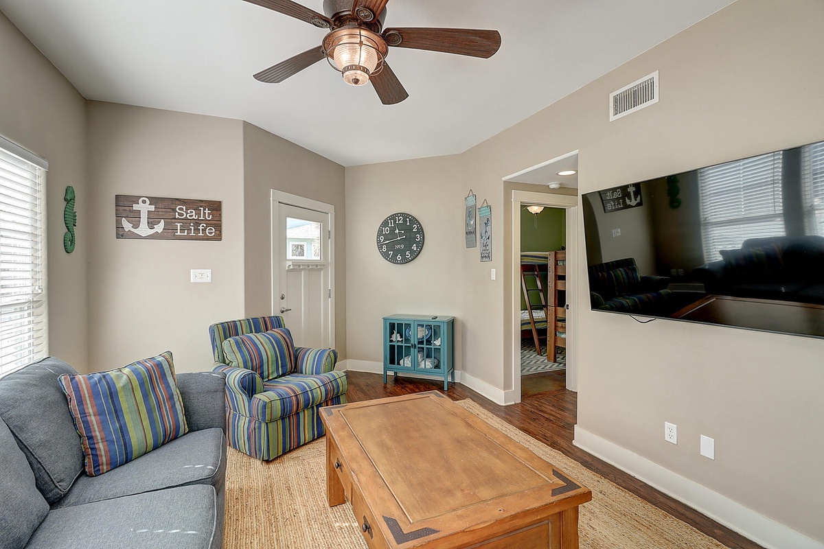 Relax in your coastal-themed living room with nautical decor, comfy seating, and a gentle ceiling fan creating the perfect beach house atmosphere.