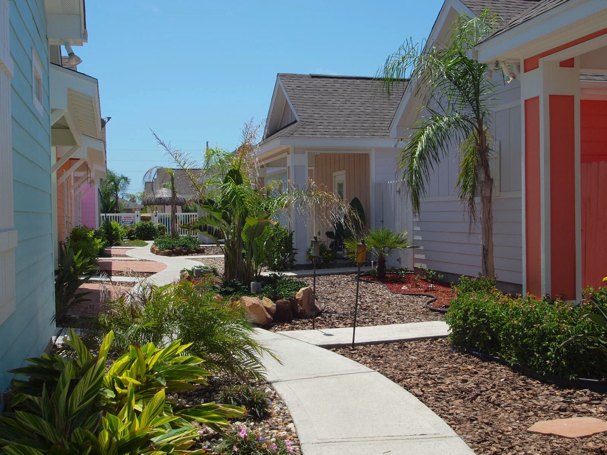 Charming tropical resort setting with colorful beach cottages surrounded by lush landscaping and winding pathways.