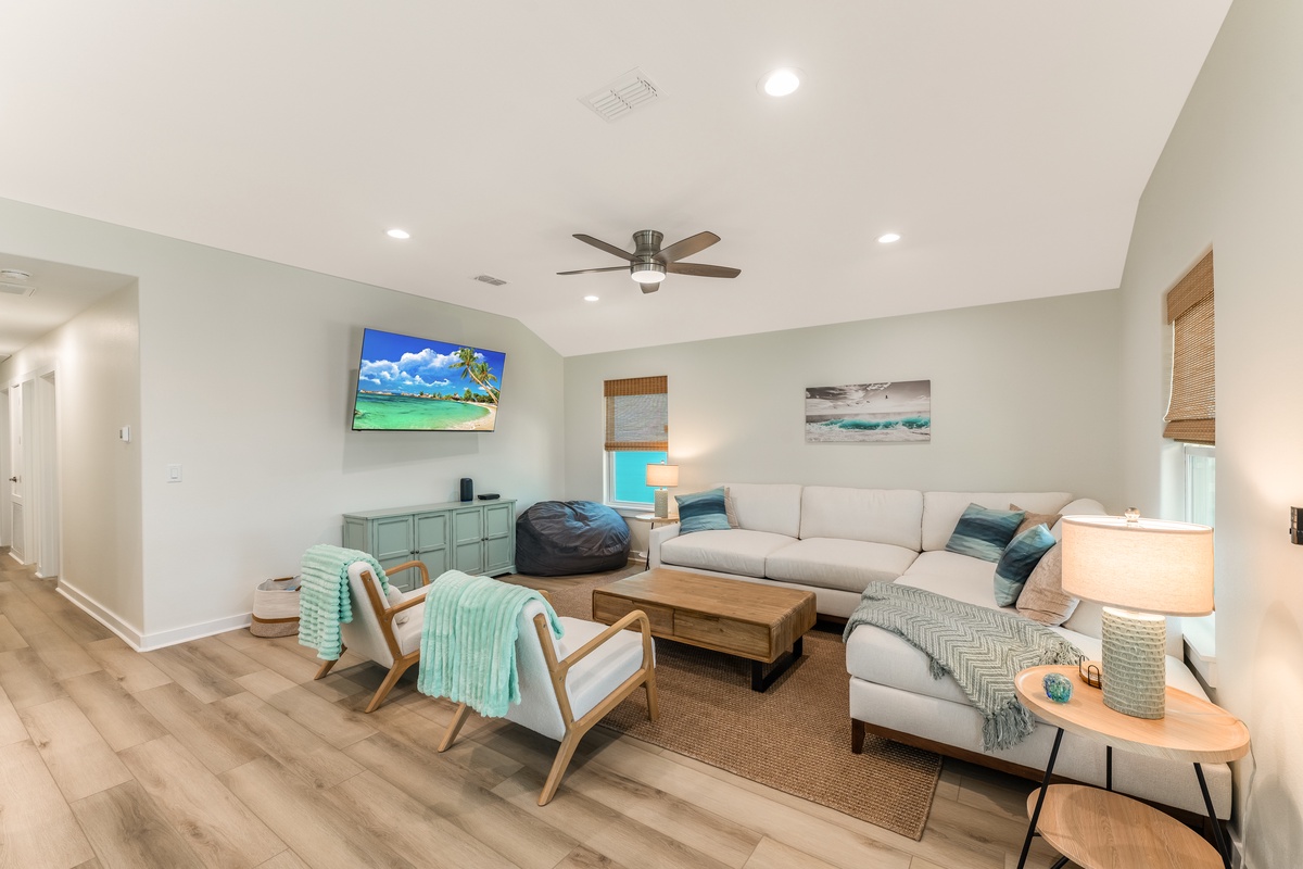 Relax in this spacious living room featuring coastal decor, plush seating, and tropical artwork that sets the perfect vacation mood.