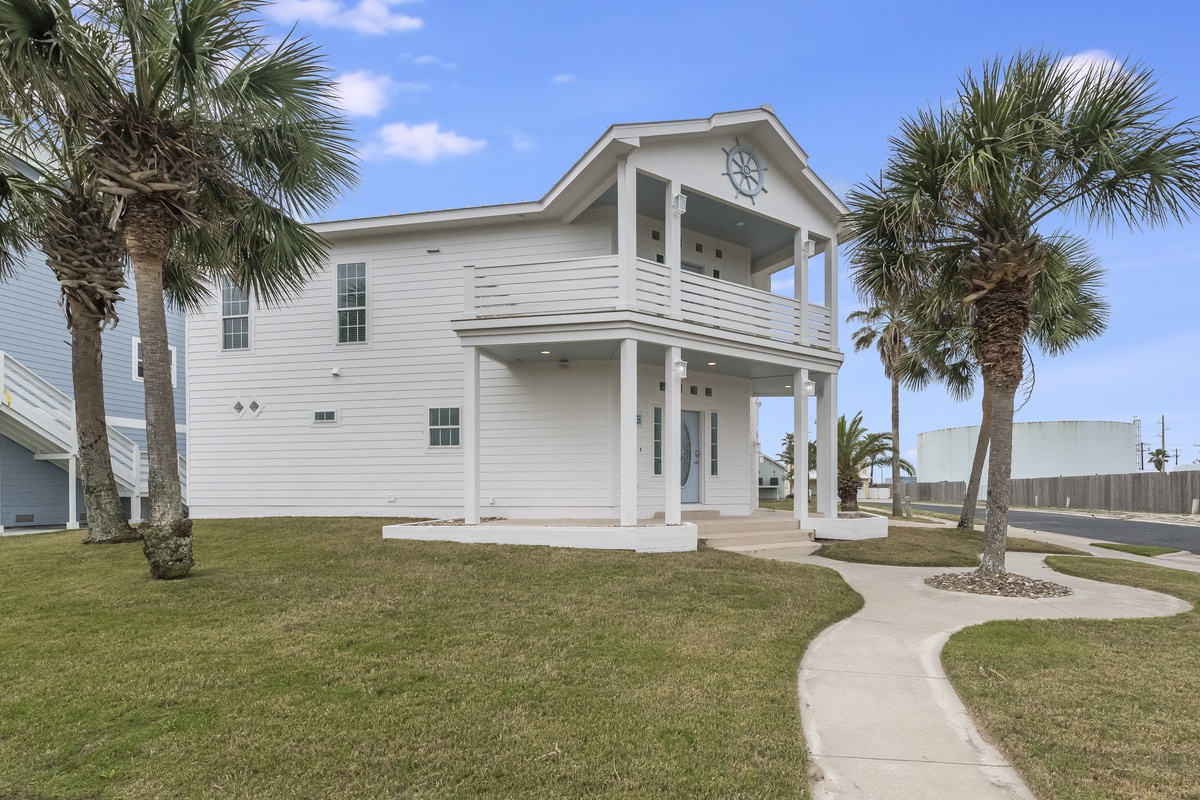 Modern coastal home featuring two-story design with covered porches and tropical palm trees in the landscaped front yard.