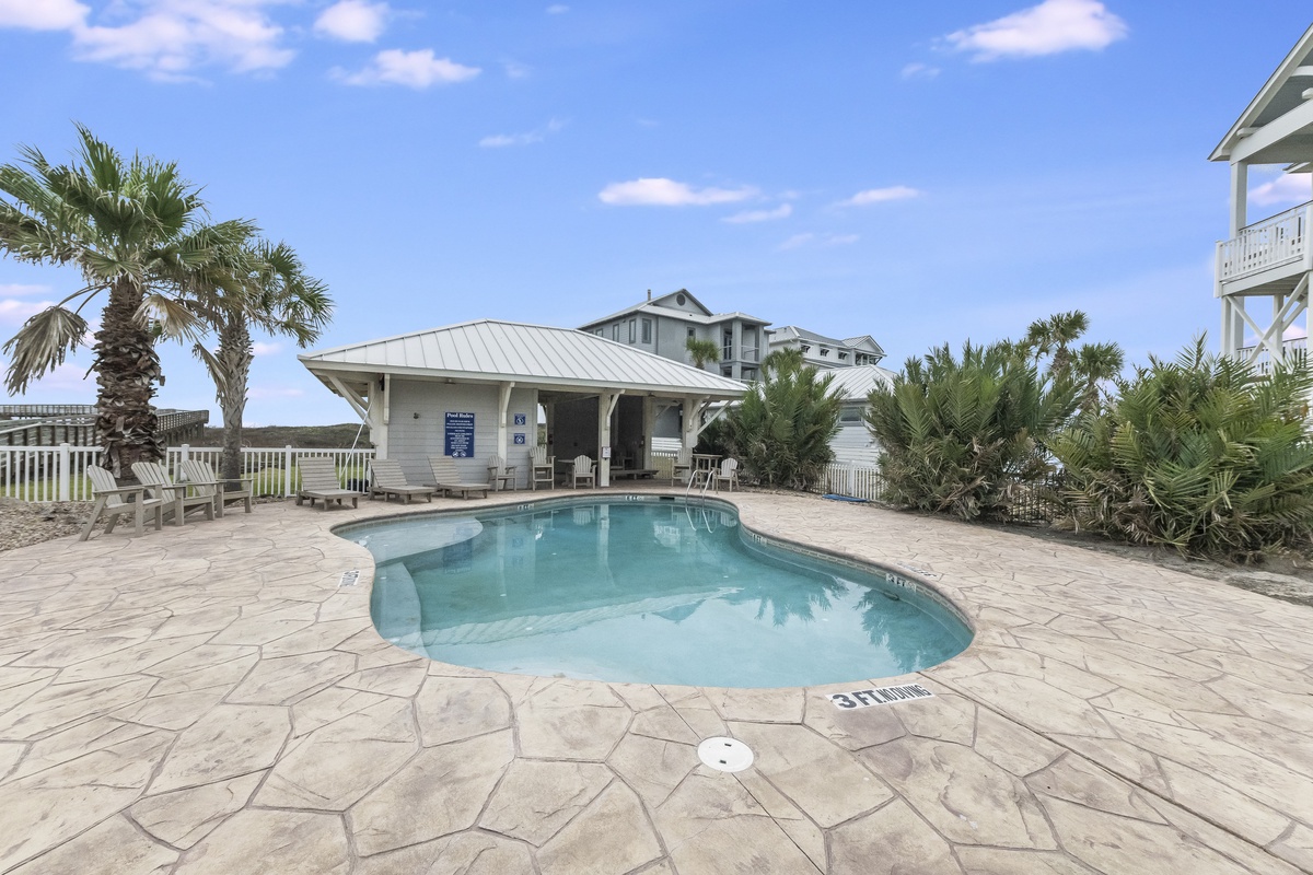 Community pool area surrounded by tropical palm trees and beautiful coastal architecture in a peaceful residential setting.