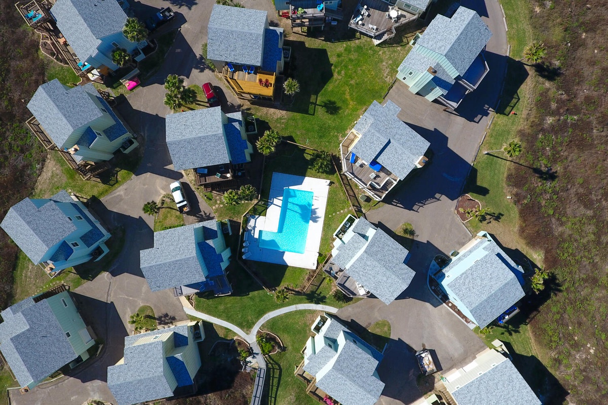 Aerial view of a peaceful residential neighborhood featuring multiple homes with landscaped yards and a shared swimming pool area.