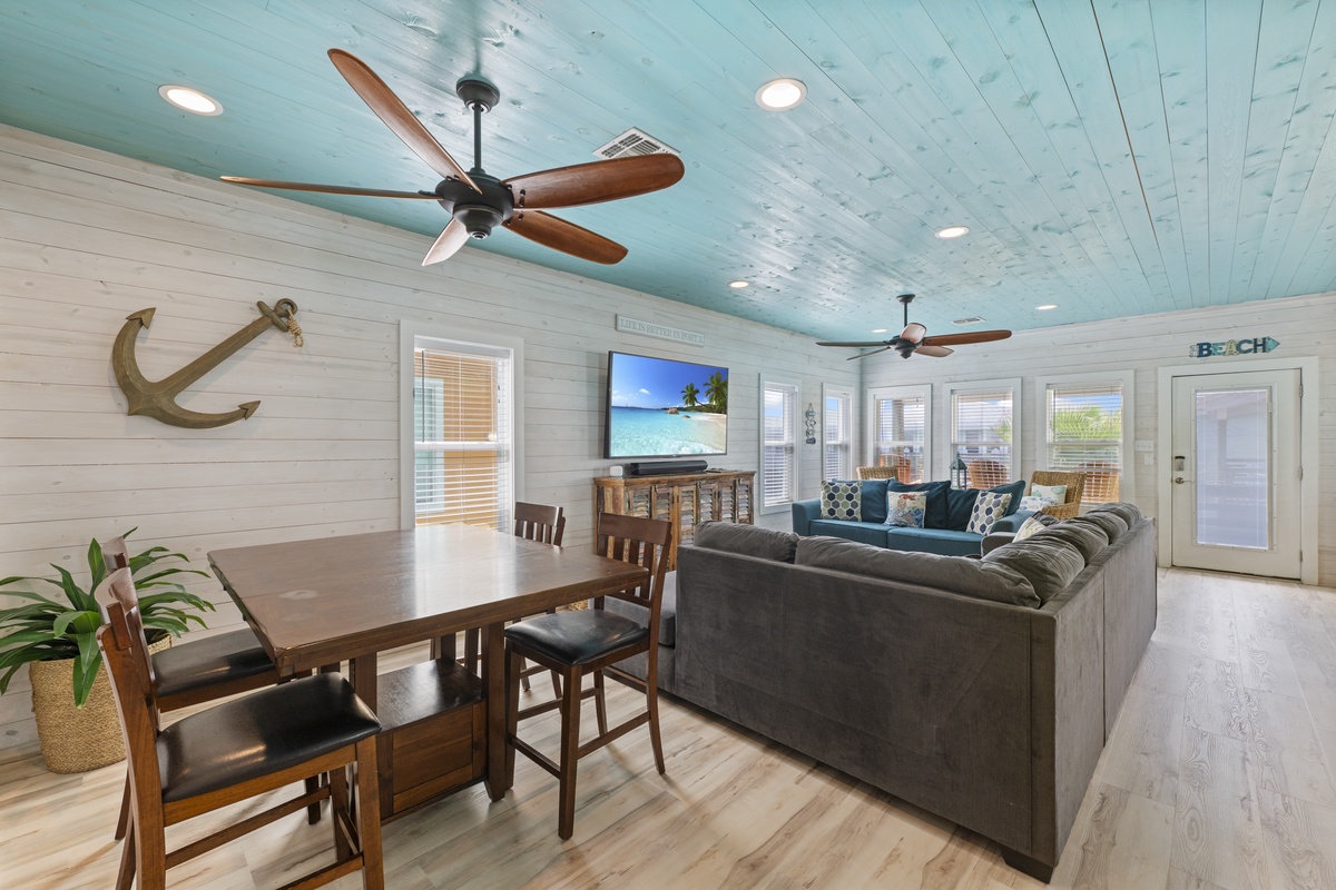 Sink into plush coastal comfort beneath breezy ceiling fans and charming turquoise ceilings. Your open-plan living and dining area invites relaxation, with beach-themed touches setting the perfect vacation mood.