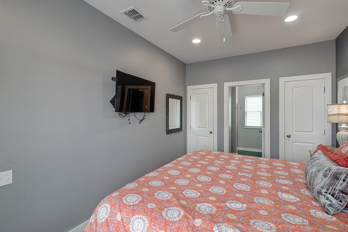 Drift off in your comfortable bedroom with ceiling fan, wall-mounted TV, and calming gray walls creating the perfect restful retreat.