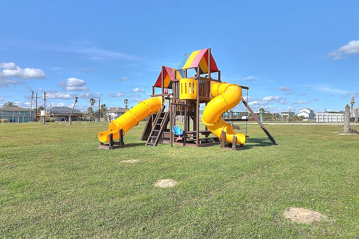 Colorful playground with slides and climbing features set on spacious green field under sunny skies.