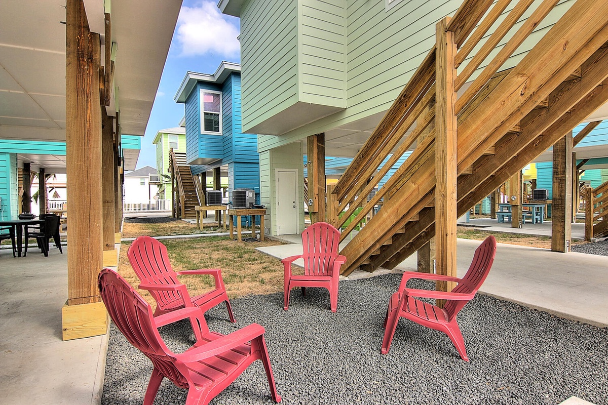 Relax in bright coral chairs beneath your covered patio, enjoying the breezy coastal atmosphere and colorful beach house surroundings.