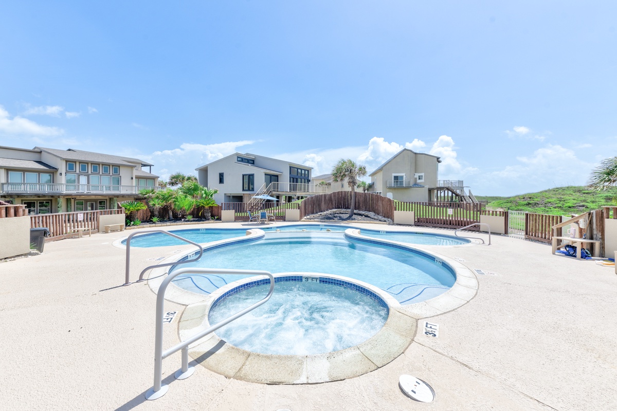 Modern beachside community featuring a curved swimming pool with integrated hot tub, surrounded by contemporary vacation homes and natural dunes.
