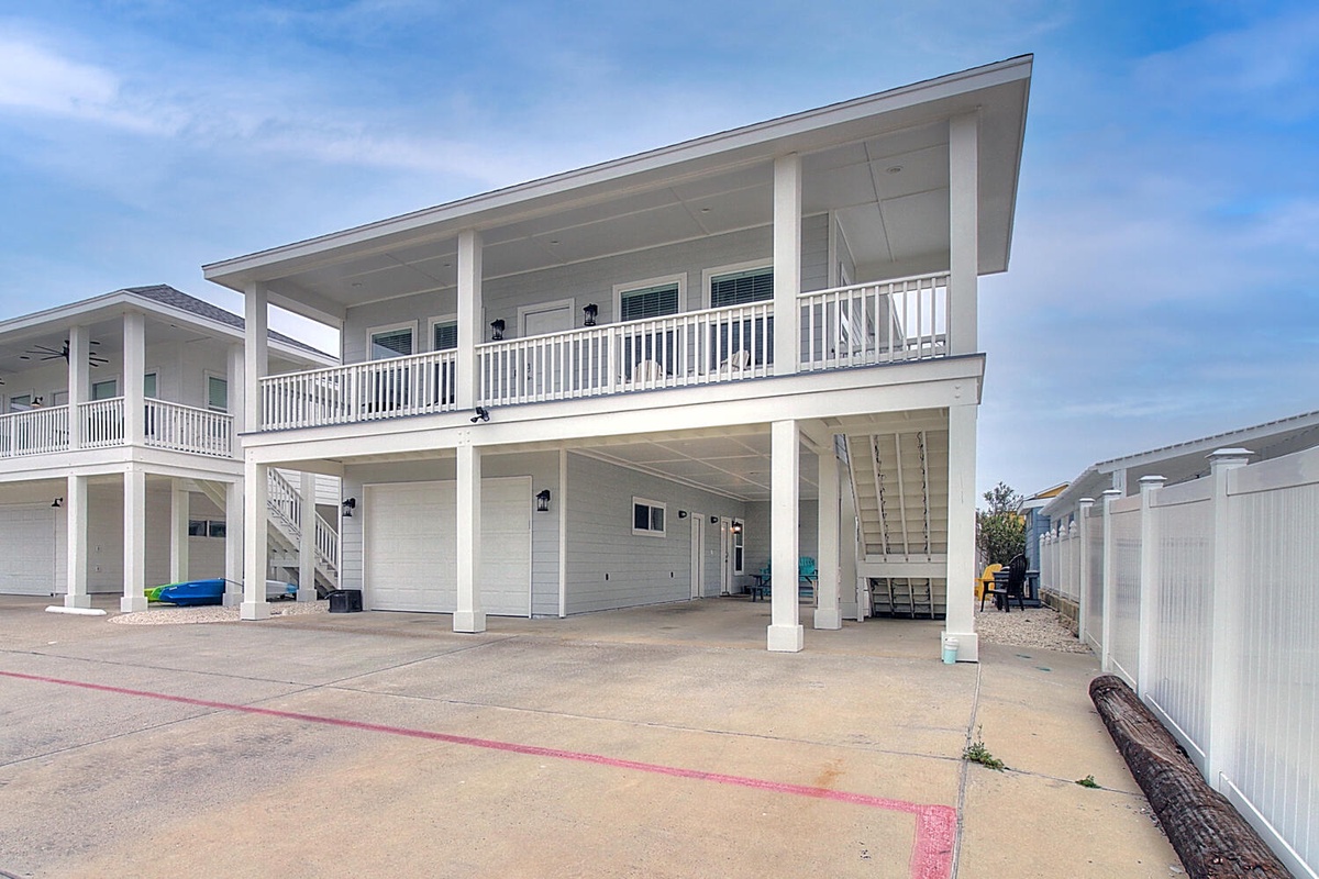Modern two-story vacation rental featuring covered parking and balcony access in a clean, coastal-style design.