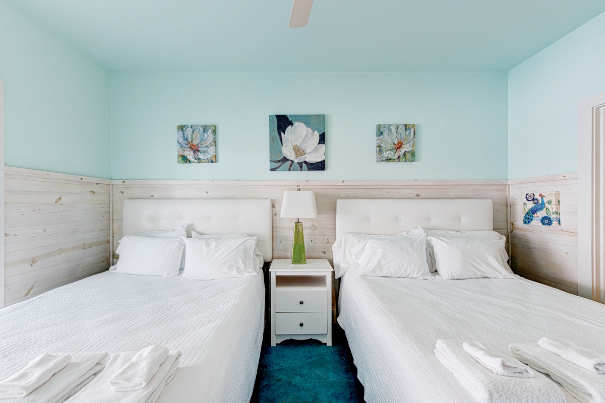 Rest peacefully in your twin-bed room featuring crisp white linens, calming mint walls, and charming floral artwork that creates a serene seaside retreat.