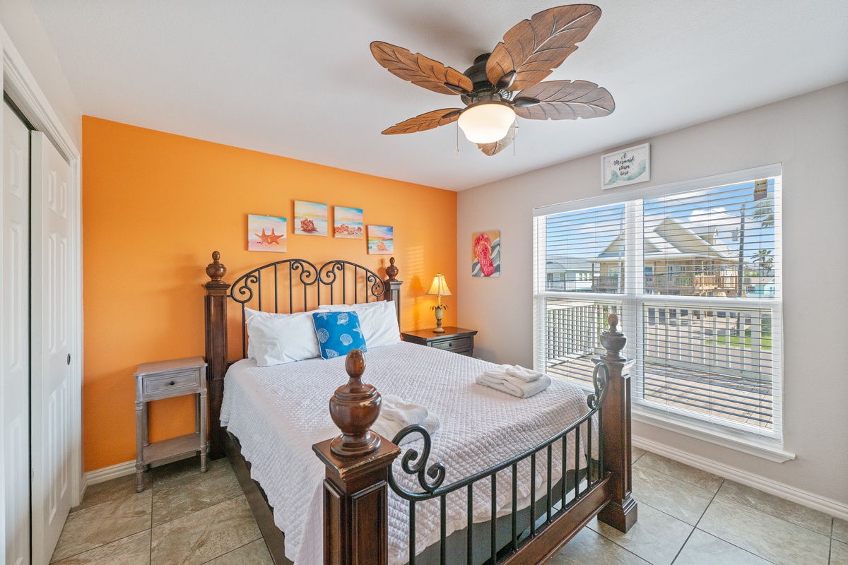 Your bright bedroom features a tropical ceiling fan and cheerful orange accent wall, creating the perfect coastal retreat atmosphere.