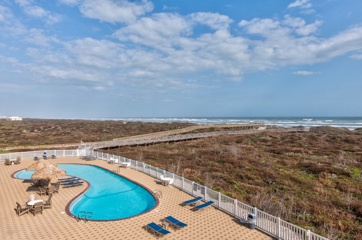 Oceanfront pool deck with direct beach access via boardwalk. The kidney-shaped pool overlooks coastal dunes and Atlantic shoreline.
