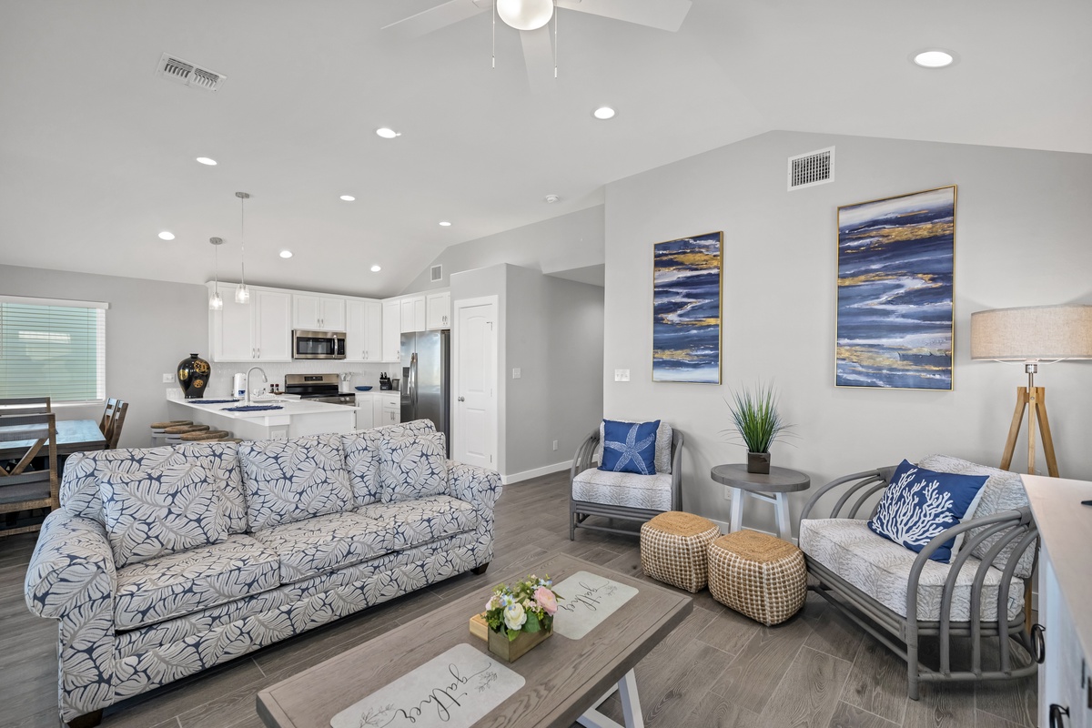 Relax in your bright open-concept living space with coastal-themed furnishings, modern kitchen, and stylish blue accents throughout.