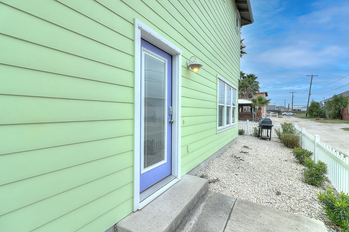 Charming green beach house with coastal landscaping and convenient street access in a peaceful residential neighborhood.