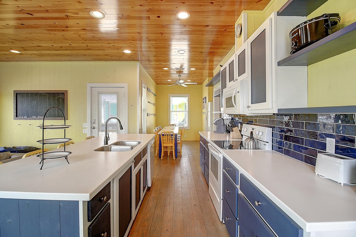 Your spacious kitchen awaits with gleaming countertops, modern appliances, and stunning blue tile backsplash under warm wood ceilings.