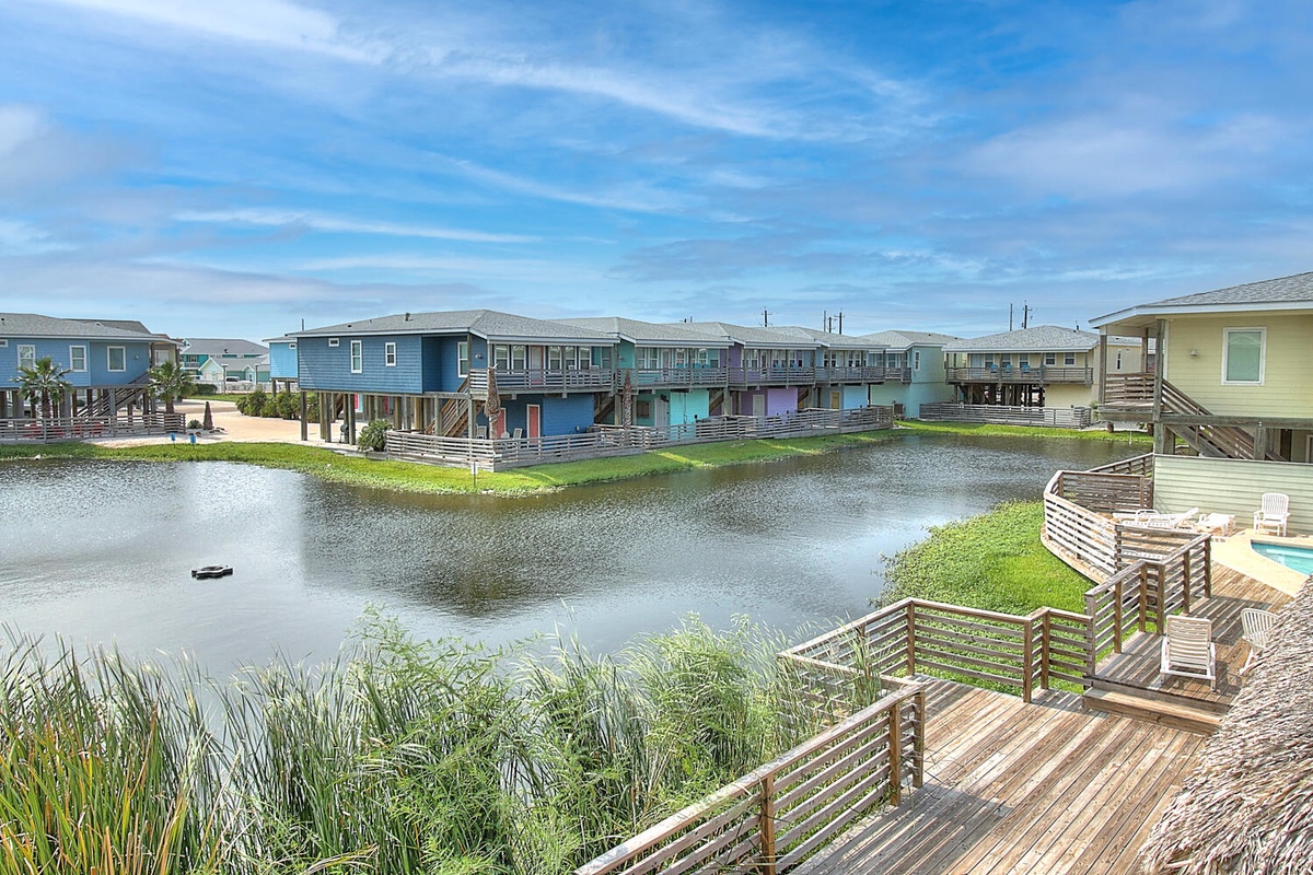 Waterfront retreat community with colorful raised homes surrounding a tranquil lagoon under bright coastal skies.