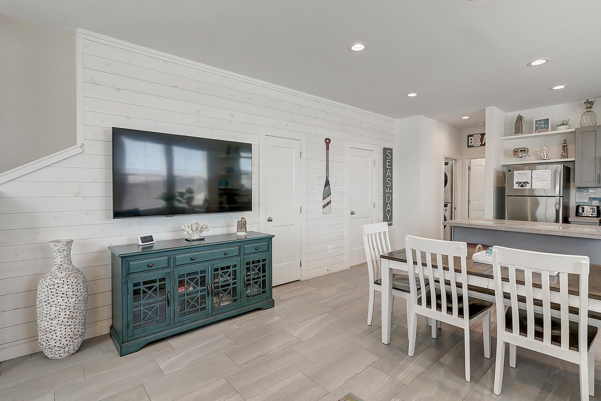 Relax in your open-concept living space featuring coastal charm with shiplap walls, a vibrant media console, and seamless flow to the modern kitchen.