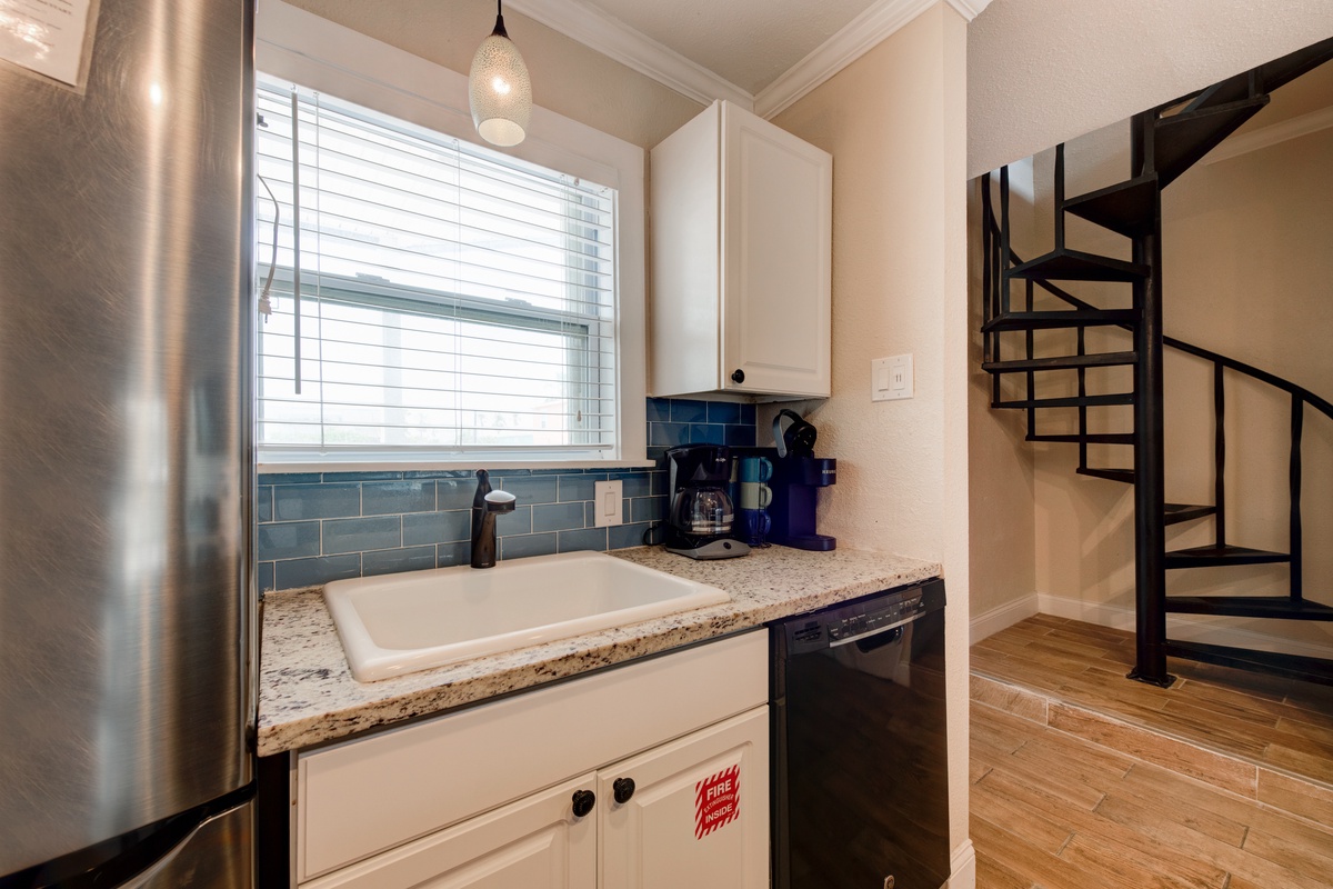 Your compact kitchen features granite countertops, subway tile backsplash, and stainless steel appliances, with a striking spiral staircase nearby.