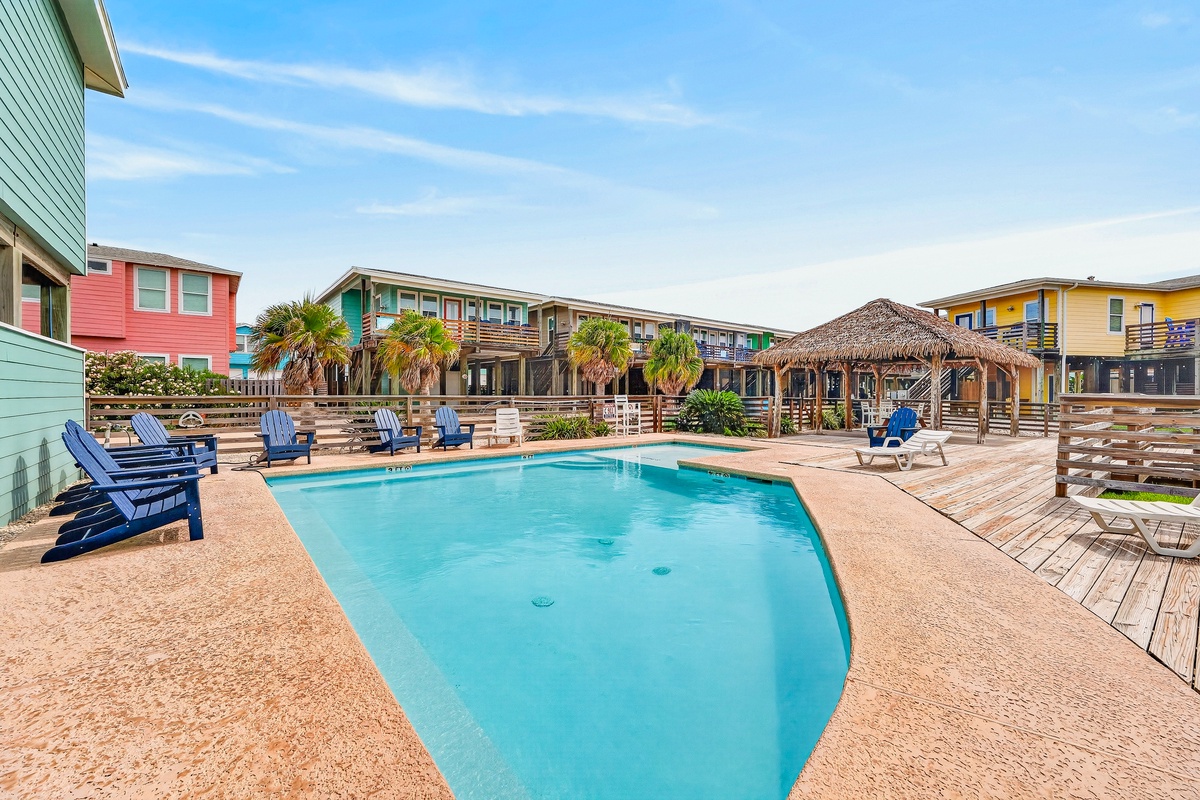 A vibrant coastal community featuring a sparkling pool surrounded by colorful beach cottages, palm trees, and thatched-roof cabanas—your perfect retreat for sunshine and relaxation.