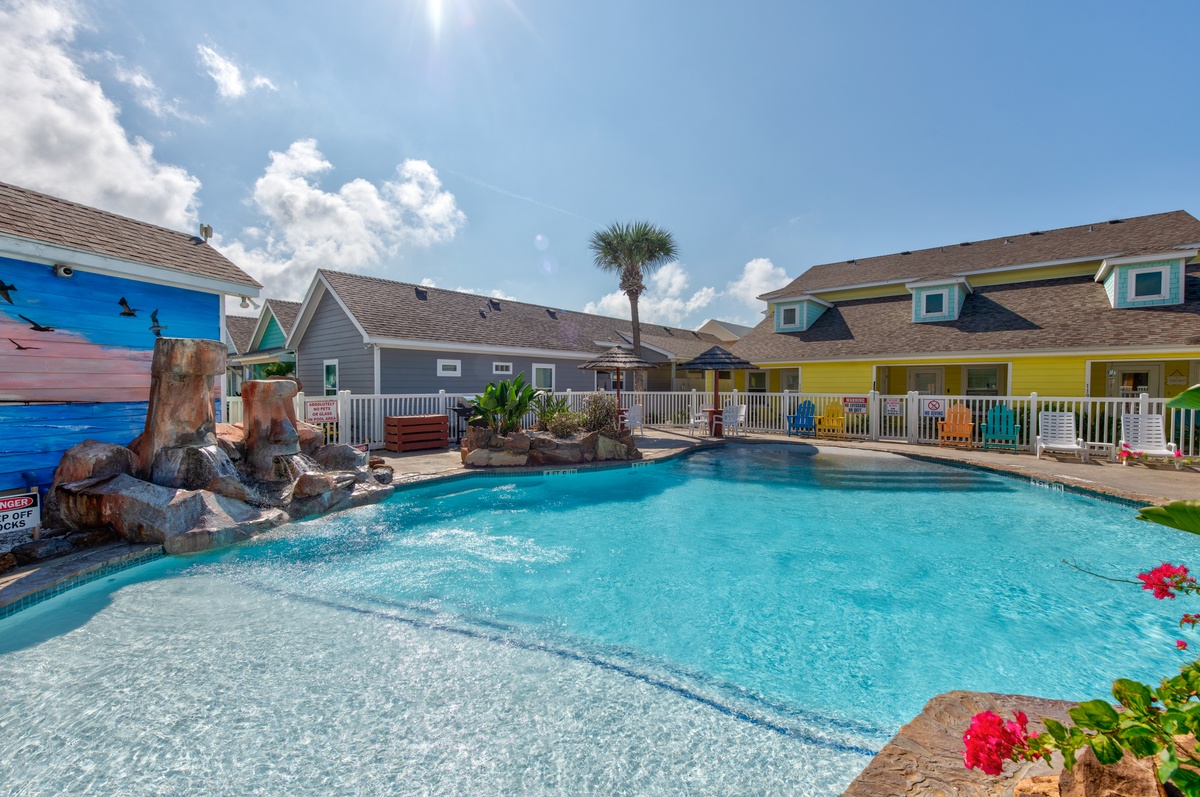 Colorful beachside resort featuring a crystal-clear swimming pool with tropical landscaping and charming coastal cottages.