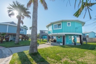 Bright turquoise beach house on stilts surrounded by swaying palm trees creates your perfect tropical escape.