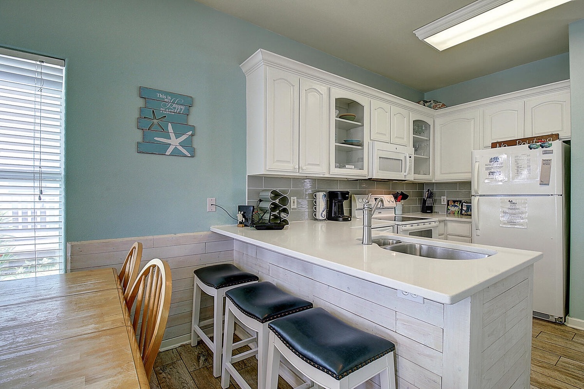 Your coastal-inspired kitchen features crisp white cabinets and a breakfast bar where you can sip morning coffee while planning beach adventures.