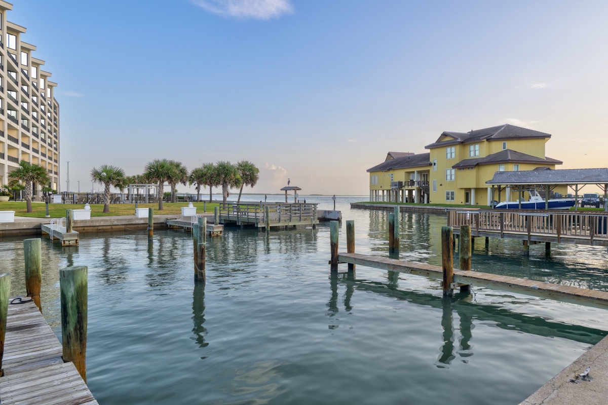 Waterfront property featuring private boat docks and marina access, set against calm bay waters. Palm-lined grounds provide coastal ambiance beside modern accommodations and a charming yellow waterfront residence.