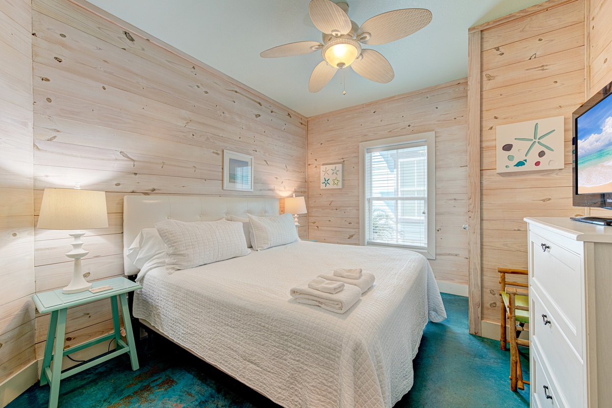 Sink into coastal comfort in your private bedroom with rustic wood walls, soft linens, and gentle ceiling fan breeze.