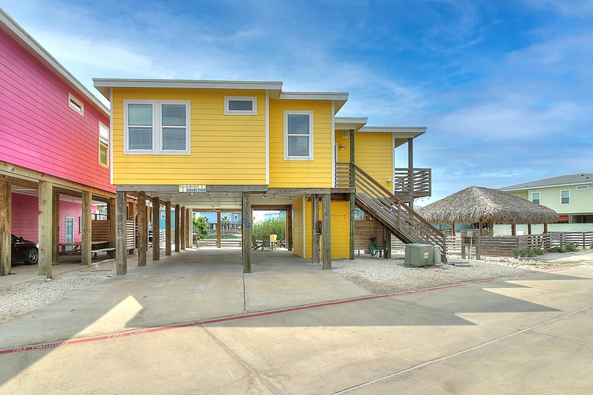 A vibrant yellow beach house with elevated design sits among colorful coastal homes, offering convenient parking underneath and modern outdoor living spaces.