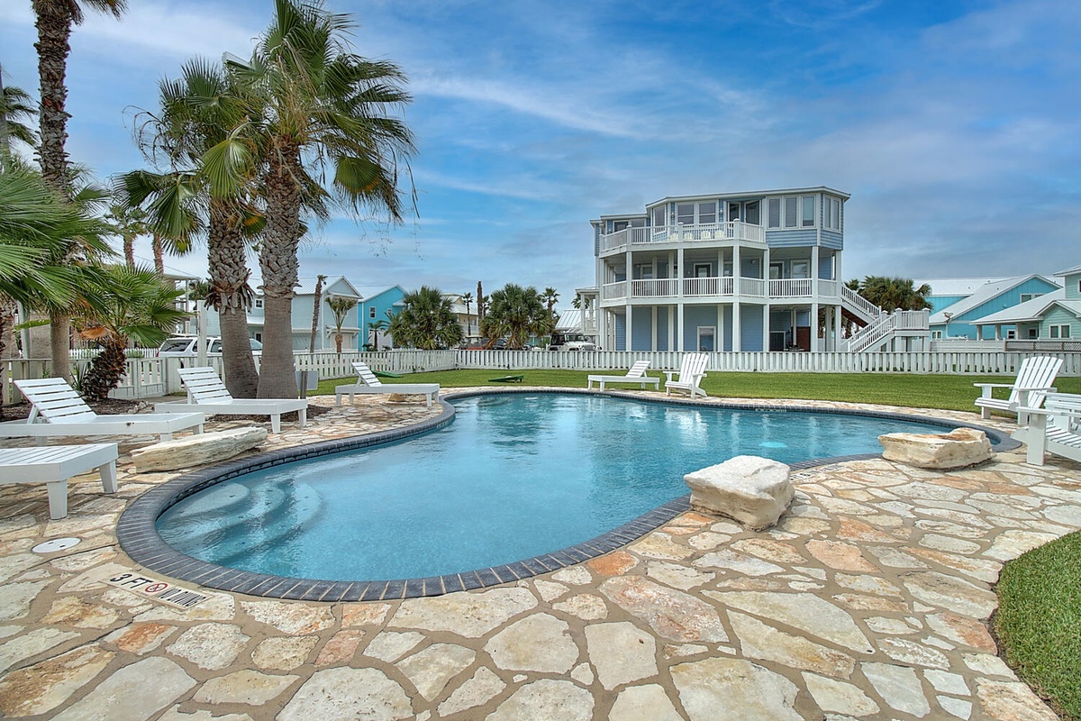 Sparkling pool with stone deck and tropical palms creates the perfect backdrop for your coastal getaway.