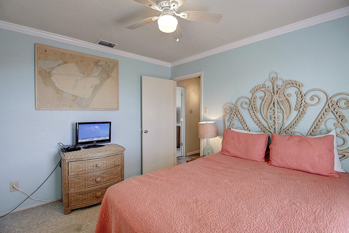 Rest easy in your coastal-inspired bedroom with coral bedding, decorative headboard, and gentle ceiling fan breeze keeping you comfortable.