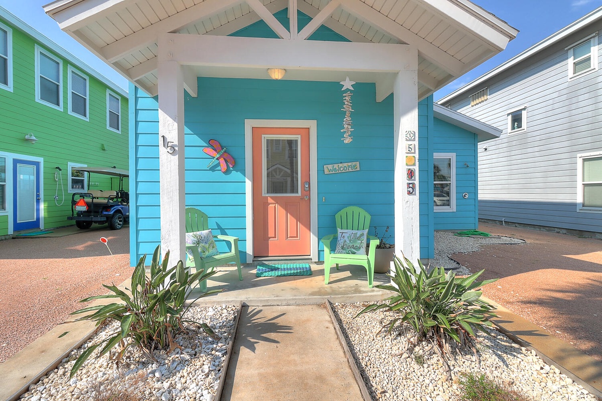 Bright coastal cottage with turquoise siding and covered porch featuring cheerful beach decor and welcoming seating area.