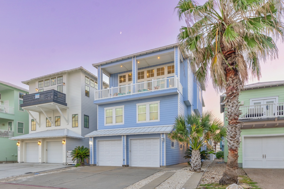 Charming coastal blue home with palm trees and covered balconies in a colorful beachside neighborhood.