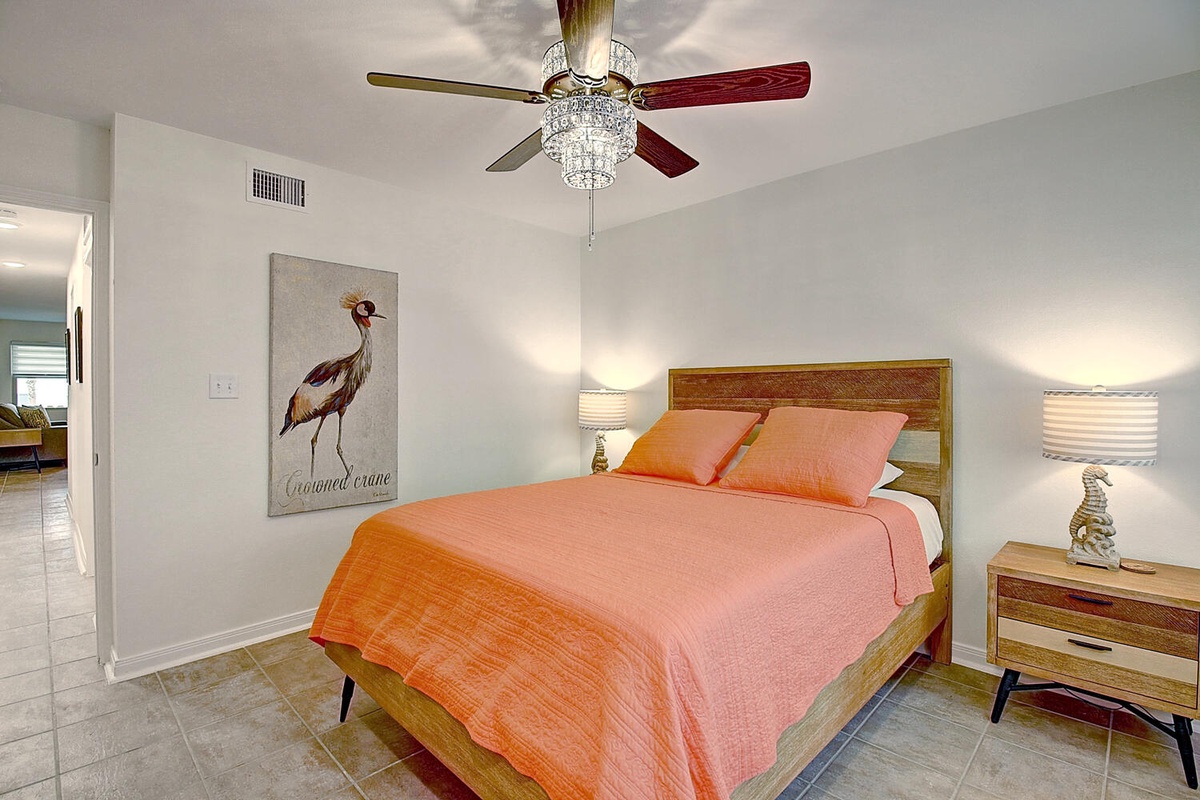 Your stylish bedroom features a comfortable bed with vibrant coral linens, elegant ceiling fan, and charming coastal artwork to ensure peaceful nights.