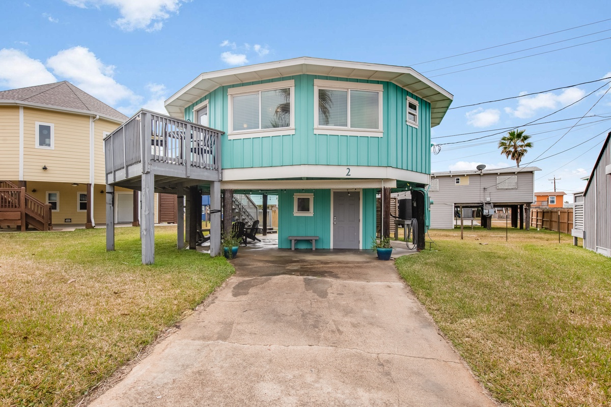 Charming turquoise beach house elevated on stilts with a welcoming covered entry and upper deck in a coastal neighborhood.