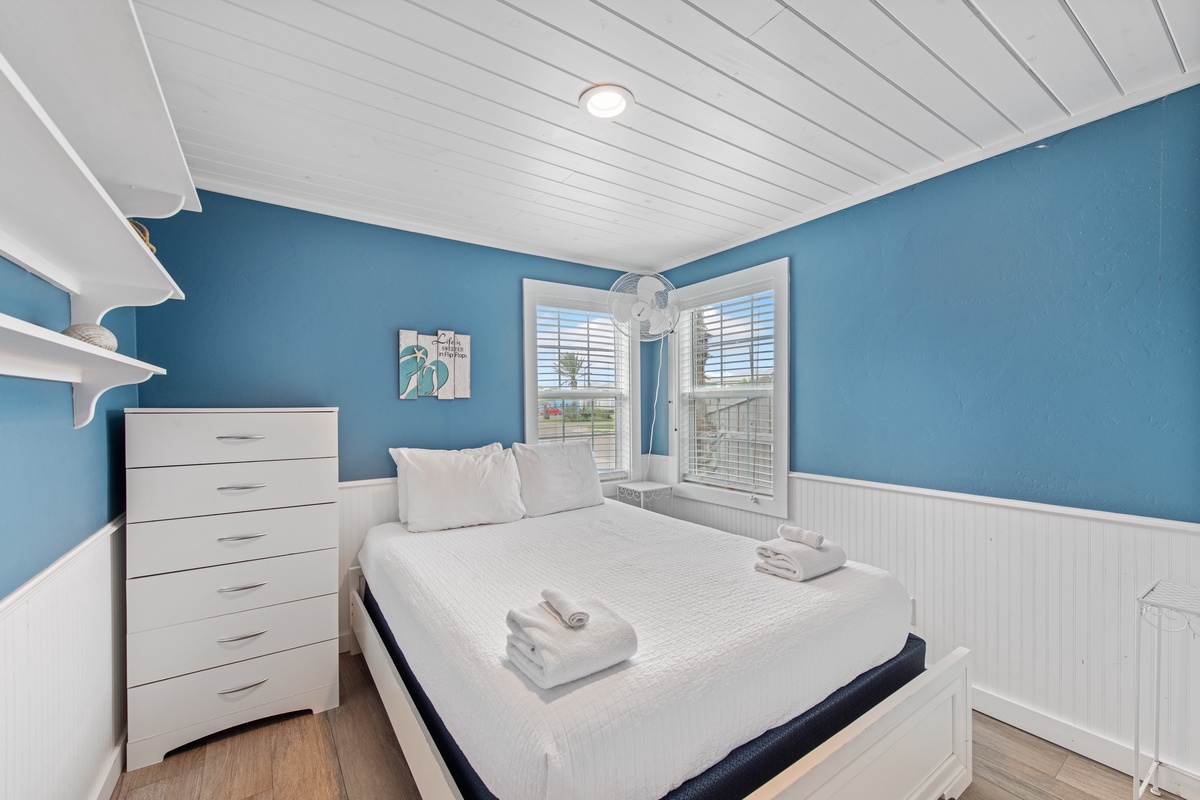 Rest peacefully in your bright coastal bedroom with soothing blue walls, crisp white linens, and natural light from bay windows.