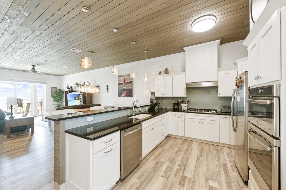 Your gourmet kitchen features sleek white cabinets, granite countertops, and stainless steel appliances beneath stunning wood beam ceilings.